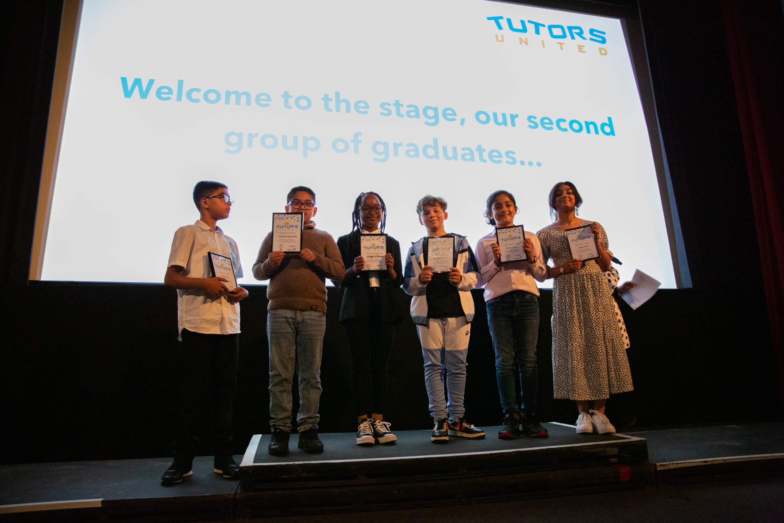 A group of pupils stands on stage with their certificates at the Tutors United Graduation 2022.